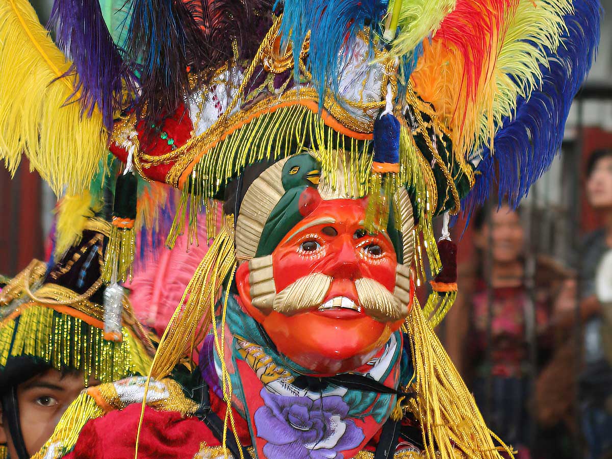 A Maya dancer wearing a vibrant mask and colorful costume, performing as part of Guatemala archaeology tours, showcasing the rich cultural heritage of the Maya civilization.