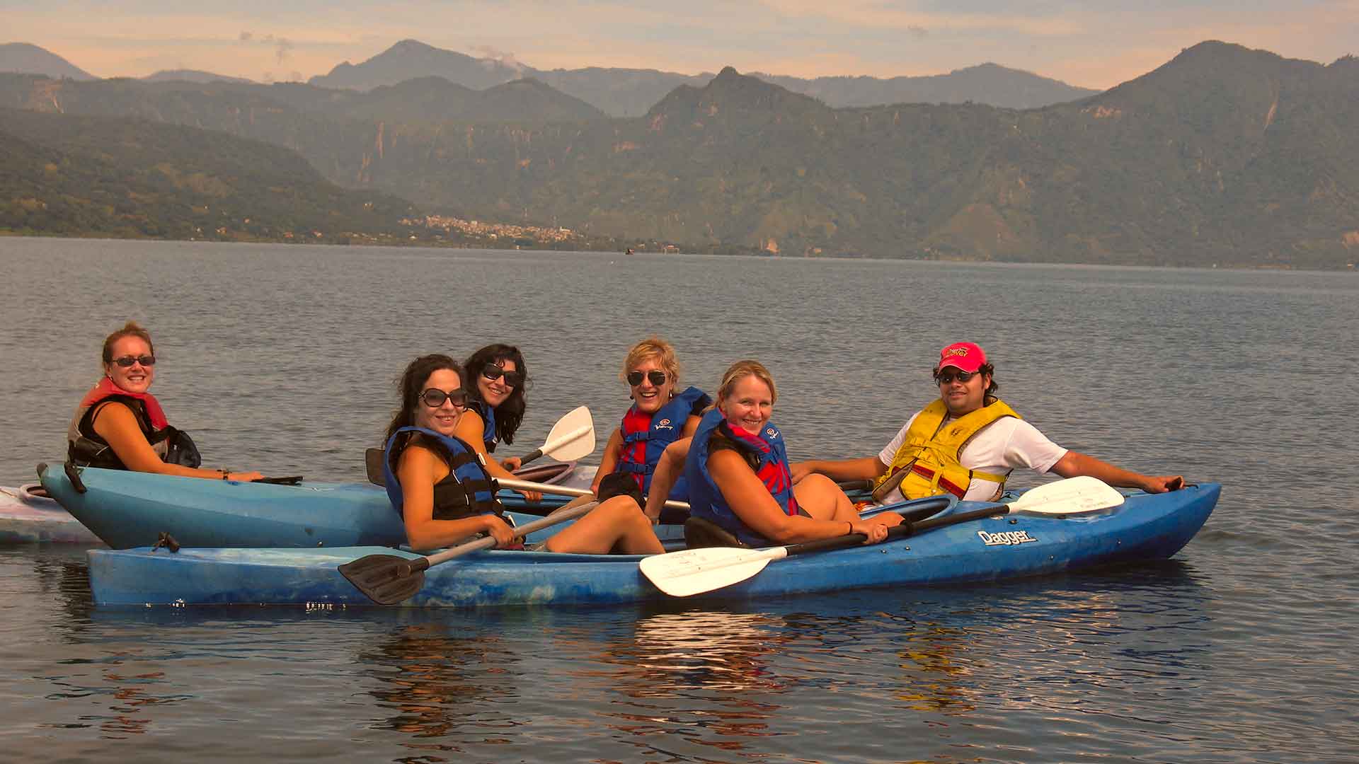 A group of women and a young man kayaking on the serene waters of Lake Atitlán, showcasing the safe and enjoyable travel experiences available in Guatemala.
