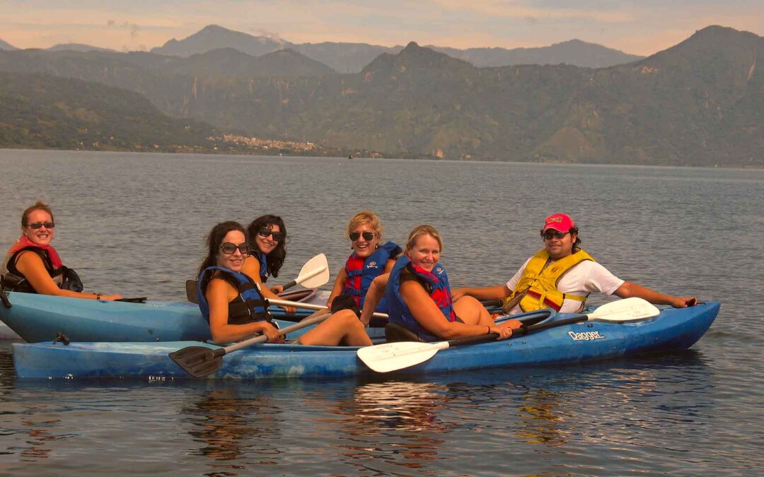 A group of women and a young man kayaking on the serene waters of Lake Atitlán, showcasing the safe and enjoyable travel experiences available in Guatemala.